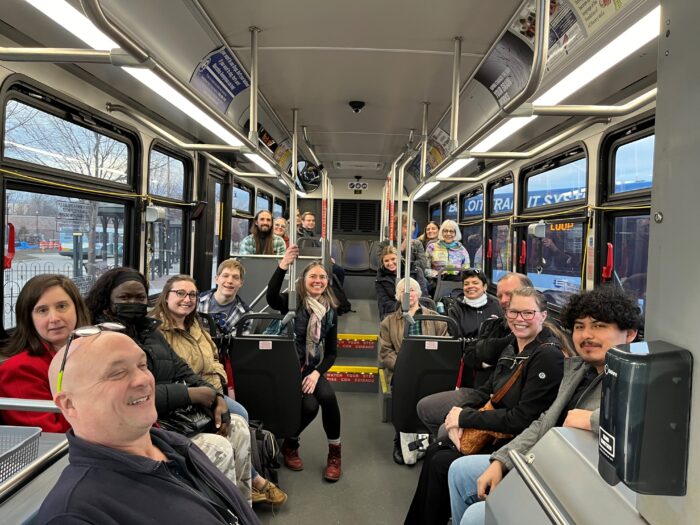 about 20 people sit on a municipal bus and smile