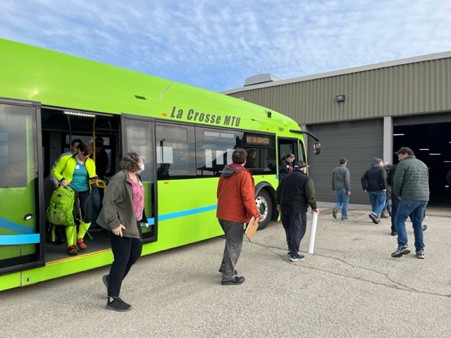 people disembarking from an electric bus that reads "La Crosse MTU" and heading into a large building