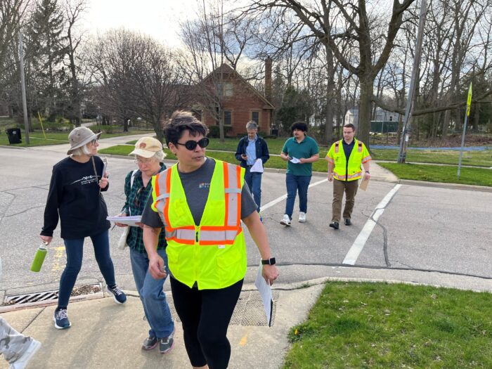 6 people holding clipboards cross a street