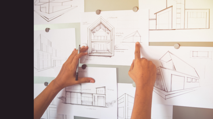 Building plans tacked on a wall, with hands holding pen to make changes
