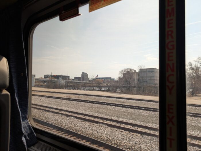 View out of Amtrak train window, looking at railroad tracks and housing beyond.