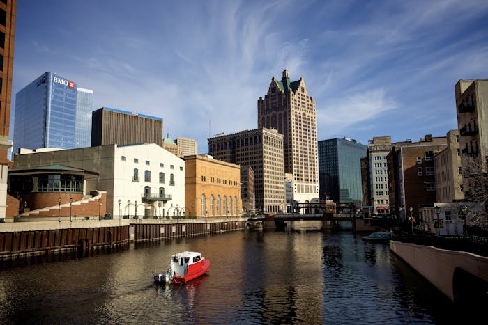 Panoramic view of Milwaukee River with iconic city buildings and a boat.