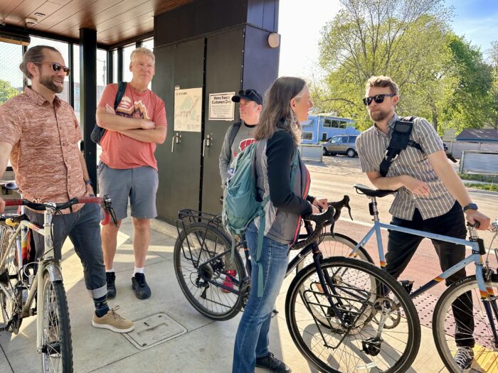 Madison Community Transportation participants wait with bikes at a bus transit stop