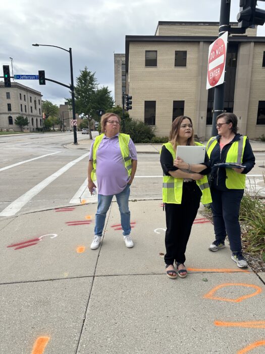 Three people stand in front of a crosswalk in downtown Green Bay during the walk-and-roll audit